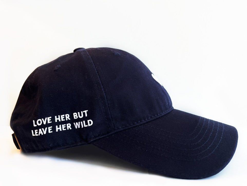 Navy blue cotton baseball cap with a white heart emblem embroidered by Atticus Poetry and "Love Her But Leave Her wild" saying embroidered